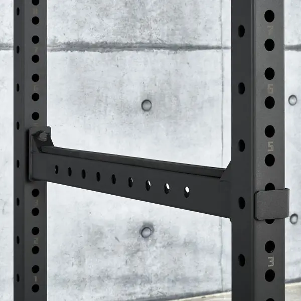 Close-up of an ATX® Power Rack 770 XL SET against a gray concrete wall. The black metal rack has multiple numbered holes for adjustable height and a secured safety bar.