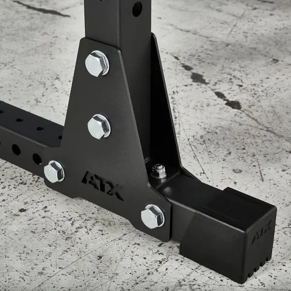 Close-up of a sturdy base with bolts and black cap on a textured gray surface, part of the ATX® Power Rack 770 XL SET. The base features several drilled holes for adjustments.