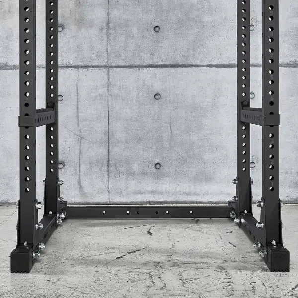 An ATX® Power Rack 770 XL SET made of black metal sits on a concrete floor against a concrete wall, featuring multiple holes for adjustable attachments, creating an industrial and minimalistic look.