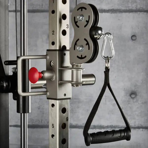 Close-up of the ATX® ERGO Stirrup Handle attached with a carabiner to a cable machine in the gym. A concrete wall is visible in the background, and weight adjustment numbers are marked on the equipment.