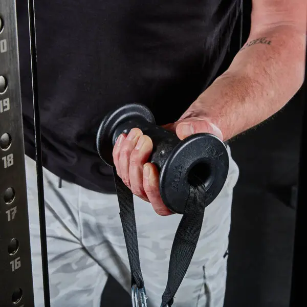 A person grips ATX® Conic Fat Grips, attached to a cable weight machine while wearing a black shirt and camouflage pants. The machine has numbered weight settings on its side.