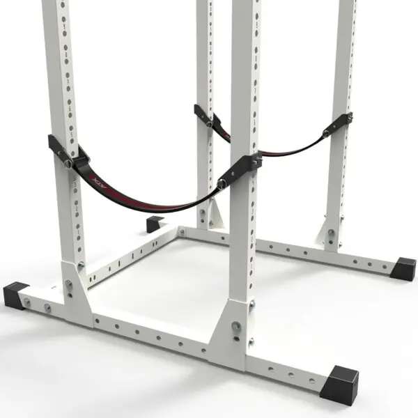 A close-up shows a gym squat rack featuring the ATX® Safety Strap 700 70cm for added security. The white rack with black accents is set on a plain gray floor, with safety straps securely attached to its structure.