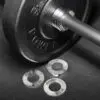 A close-up shows a black barbell weight plate labeled POWER 1 KG with three smaller silver plates nearby, branded ATX and marked 0.25 kg, 0.5 kg, and 1 kg, from the ATX® Olympic Fractional Plate Pairs collection on a dark surface.