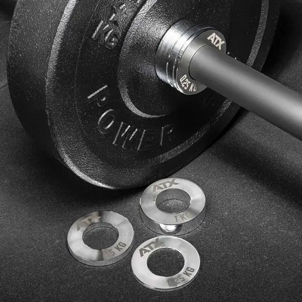 A close-up shows a black barbell weight plate labeled POWER 1 KG with three smaller silver plates nearby, branded ATX and marked 0.25 kg, 0.5 kg, and 1 kg, from the ATX® Olympic Fractional Plate Pairs collection on a dark surface.
