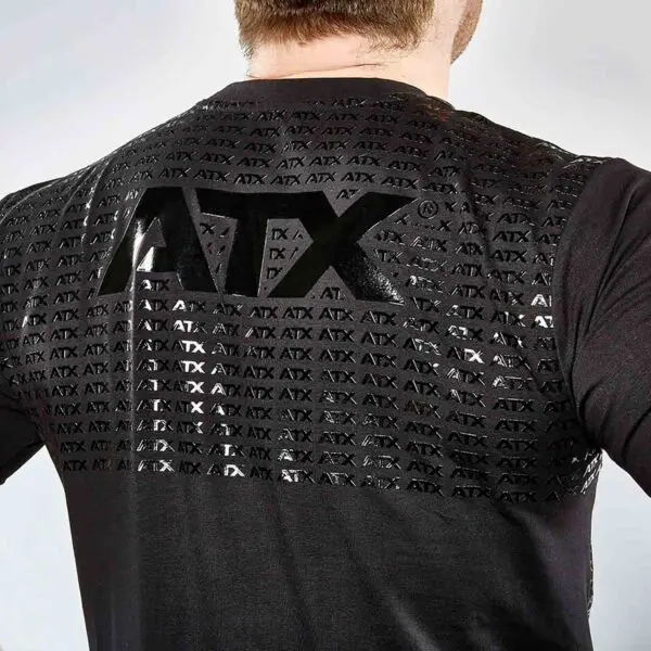 Rear view of a person wearing an ATX® Grip Shirt with black fabric and a shiny grid-like ATX logo pattern across the back, standing against a light gray background.