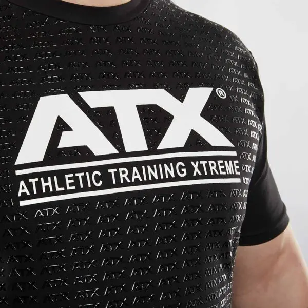Close-up of a person wearing a black ATX® Grip Shirt featuring a repeating ATX pattern. A larger ATX logo and Athletic Training Xtreme text are prominently printed in white on the chest, highlighting style and strength.