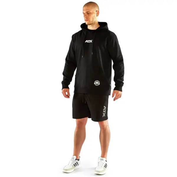 A person in an ATX® Black Hoodie and black shorts stands on a white background, wearing white sneakers with black stripes.