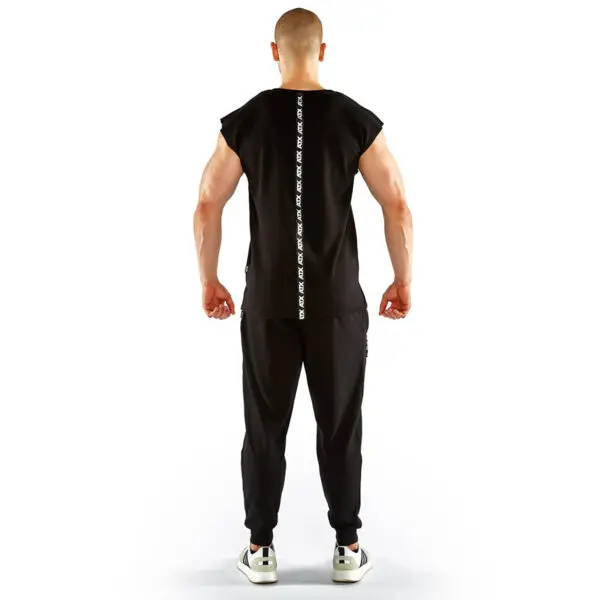 A man stands on a white background wearing the ATX® Muscle Shirt, featuring a vertical design on the back, along with black pants and white sneakers.