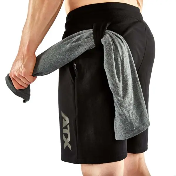 A muscular person is seen from the back, wearing ATX® Black Shorts with a gray towel hanging through the pocket.