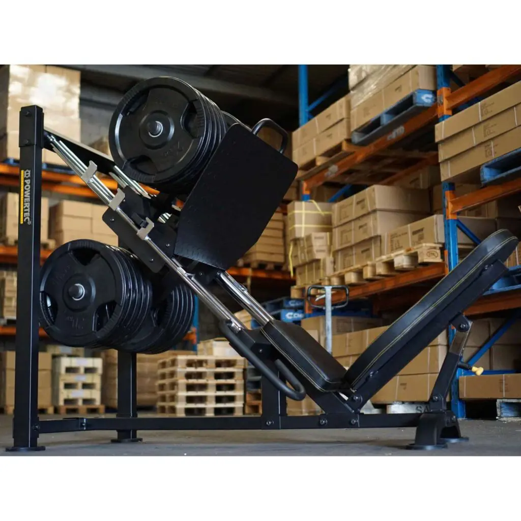 A Powertec Leg Press machine, laden with multiple weight plates, stands in a gym setting. The background reveals shelves filled with boxes and various gym equipment, creating an atmosphere of strength and perseverance.