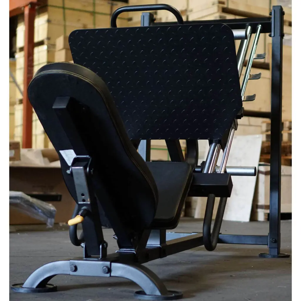 A Powertec Leg Press stands in the gym, showcasing its sleek black and metal design. The angled seat and footplate are ready for action, while weight plates adorn the sides. Wooden crates and various gym equipment complete the rugged, energetic environment.