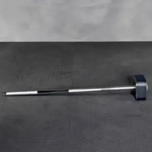 The Ironmaster Quick Lock Mace Handle, featuring a robust, long metal grip and large square rubber head, rests on a textured dark gray floor with a plain gray wall in the background.