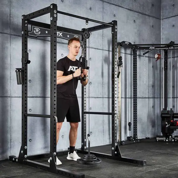 Wearing a black t-shirt and shorts, a person uses the Cable Pulley System (High) in a gym with gray concrete walls and black equipment featuring metal accents.