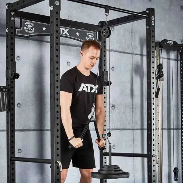 Wearing a black ATX shirt, someone performs a tricep pulldown using the Cable Pulley System (High) on an ATX power rack, set against a sleek gray concrete wall.