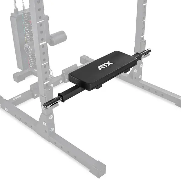 A gym setup includes a black bench pad with ATX printed on it, attached to an adjustable cable crossover machine. The ATX® Hip Thruster Attachment complements the sturdy metal frame and visible pulley system in the background.