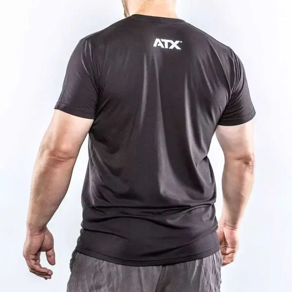 A person with short hair wears an ATX® Barbell Club T-shirt in black, ATX printed on the back, standing against a light background, arms slightly raised and facing away from the camera.