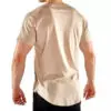A person wearing a beige short-sleeve t-shirt and black pants, viewed from the back, stands against a plain white background. The t-shirt has a curved hem. The person has short hair and their hands are relaxed by their sides.