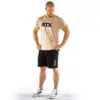 A man stands wearing a beige t-shirt with ATX printed on it, black shorts with a small ATX logo, and white sneakers with black stripes. He is looking down with hands on hips against a plain white background.