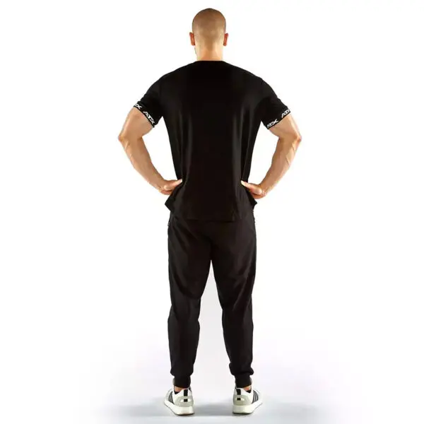 A person stands with their back to the camera, wearing an ATX® Training Shirt BLACK and pants with white sneakers. Their hands are on their hips against a plain white background.