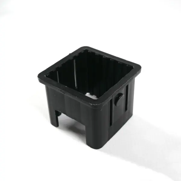 An Upright Sleeve Insert 40x40, a black rectangular plastic container with open ends and a button-like feature on one side, stands on a white surface.