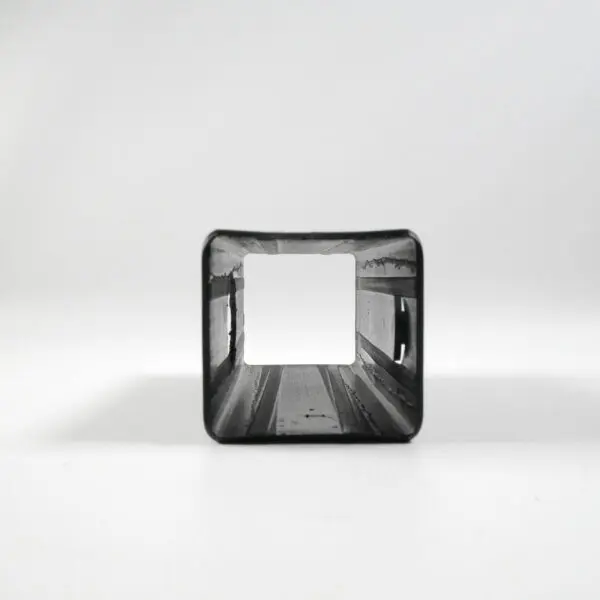 The Upright Sleeve Insert 40x40x120, a square metal pipe with an open end facing the viewer, reveals its hollow interior against a white background. It casts a soft shadow on the surface.