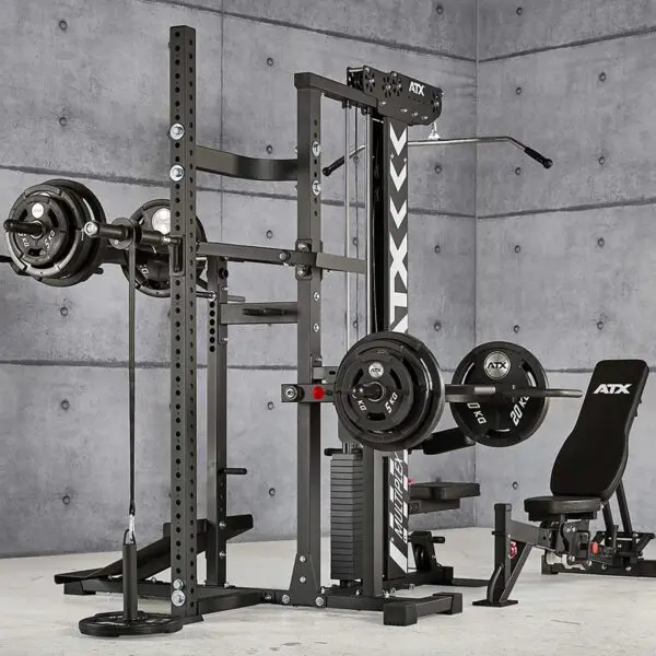 The ATX® MultipleX Multi Gym - 700 is a home gym setup, complete with a multifunctional weightlifting station. It includes a squat rack, bench press, cable pulleys, and various weight plates attached and stored on the equipment against a concrete wall background.