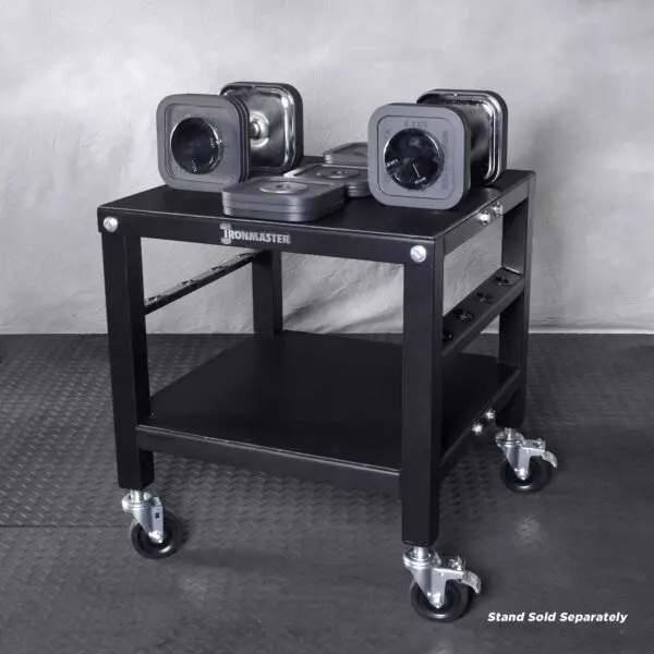 The Ironmaster 75 LB Quick-Lock Adjustable Dumbbell Set, without the stand, is organized on a black wheeled rack featuring two levels: dumbbells on top and weight plates below. The floor has a textured rubber mat pattern.