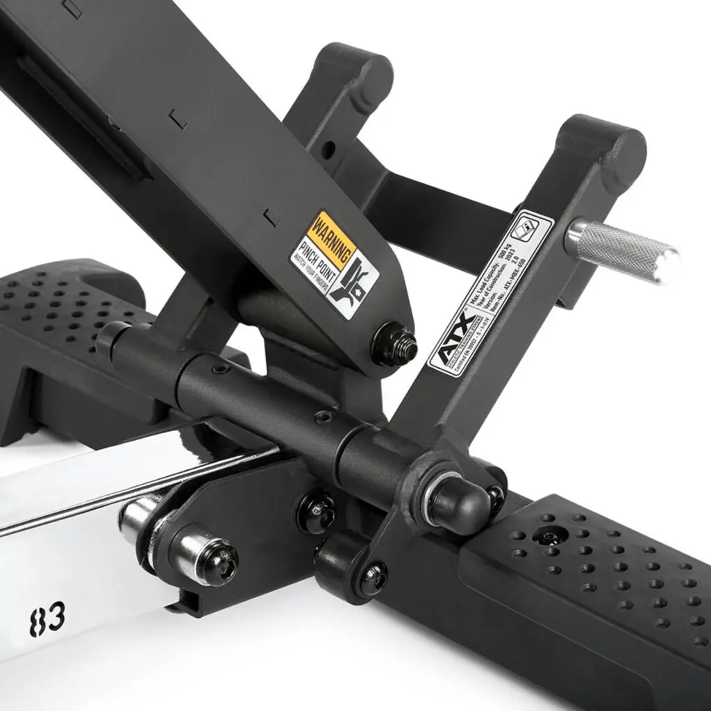 Close-up of a black adjustable bench support mechanism, highlighting its fid bench versatility. The image showcases various metal components, warning labels, and a handle grip. The perforated platform ensures traction, while the sleek bench frame provides sturdy support for any workout routine.