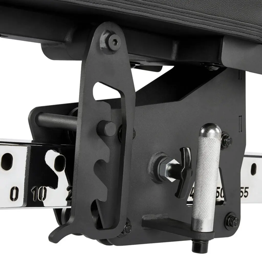 Close-up of a black adjustable mechanism on a fid bench, featuring a textured silver handle and numbered metal rail for precise positioning. The apparatus includes a series of gears and screws for fine-tuning the bench settings.