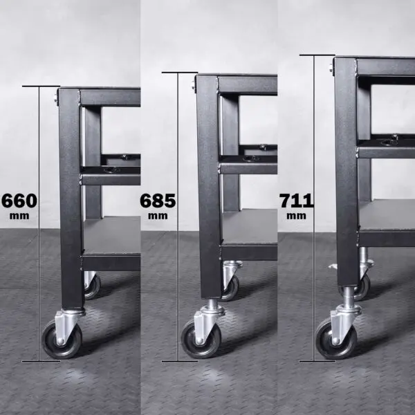 Three images of the Ironmaster QLDB Stand PRO, a metal cart with wheels, are displayed side by side showcasing it at heights of 660 mm, 685 mm, and 711 mm. The floor has patterned grey tiles and the cart features two sturdy shelves.