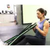 A woman in athletic wear sits on a gym floor, using the Spud Inc Infinity Loop for an arm workout. She appears focused, surrounded by visible gym equipment in the background.