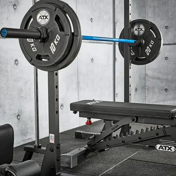 An ATX® Smith Machine 500 setup featuring a black adjustable bench, barbell with 20 kg and 10 kg plates on each side, set against a gray concrete wall and padded flooring, ideal for areas with low ceilings at just 198 cm high.