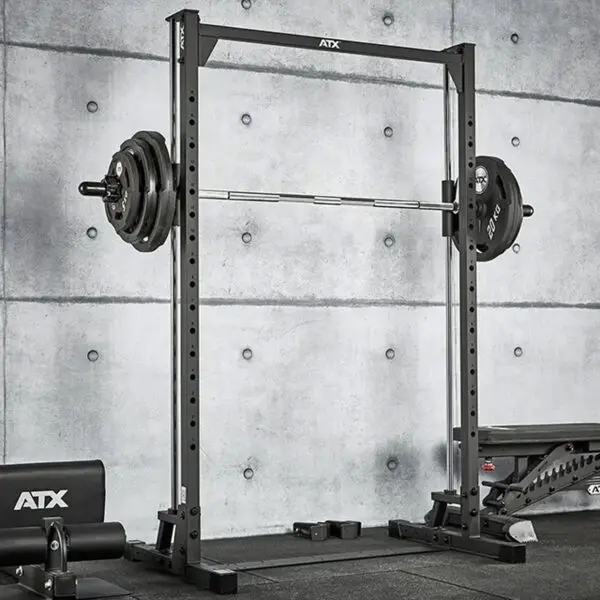 The ATX® Smith Machine 500, designed for low ceilings at 198 cm, is set up in a gym with a concrete backdrop, alongside a bench and other exercise equipment.