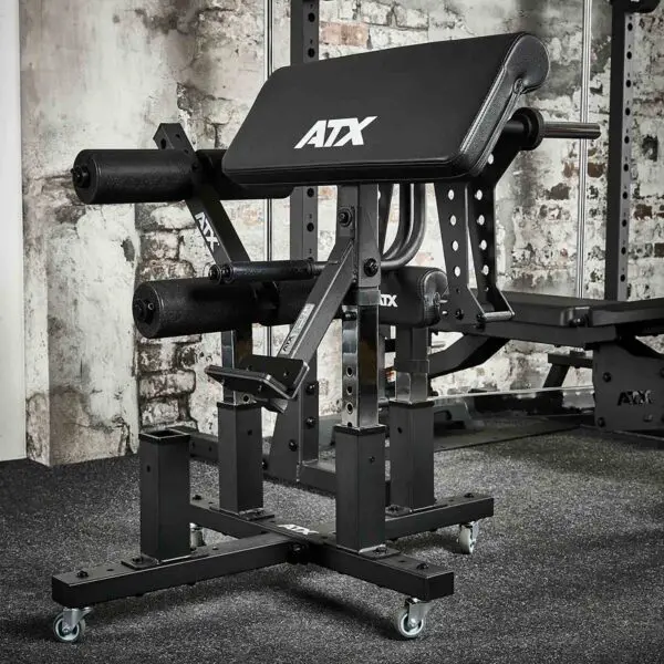An ATX® Attachment Storage Rack is set against exposed brick walls in a room. It features padded supports, an adjustable frame, and multiple padded bars for leg workouts. The floor is carpeted in dark gray.