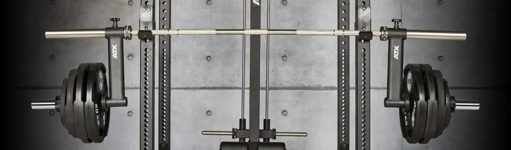 A barbell loaded with weight plates on a rack, in front of a gray textured wall.