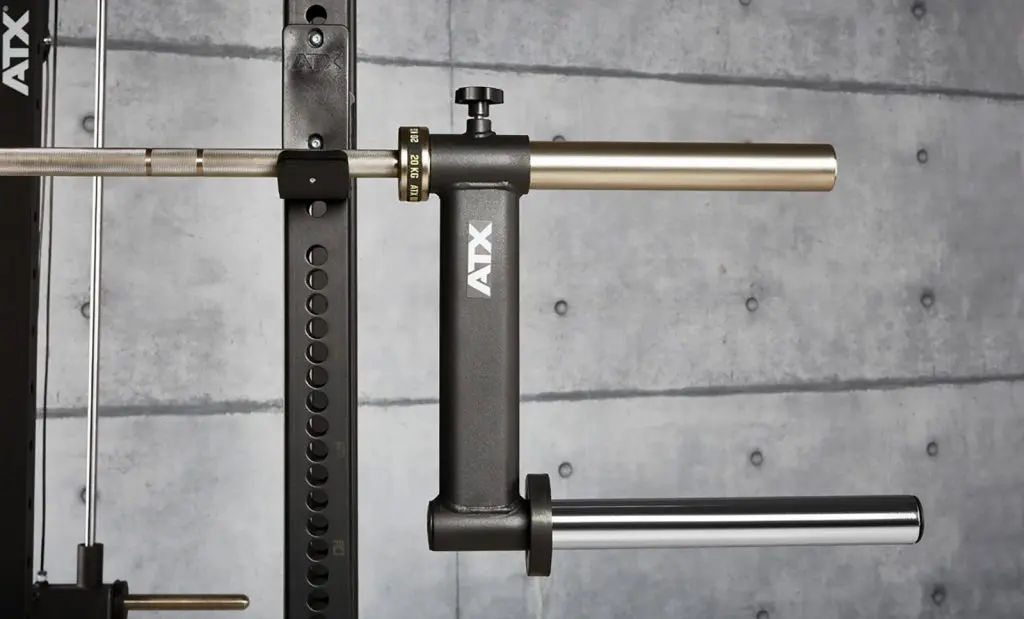 Close-up of a gym setup featuring a barbell attached to a squat rack with an ATX landmine attachment. The attachment is black with metallic handles, and the background is a concrete wall.