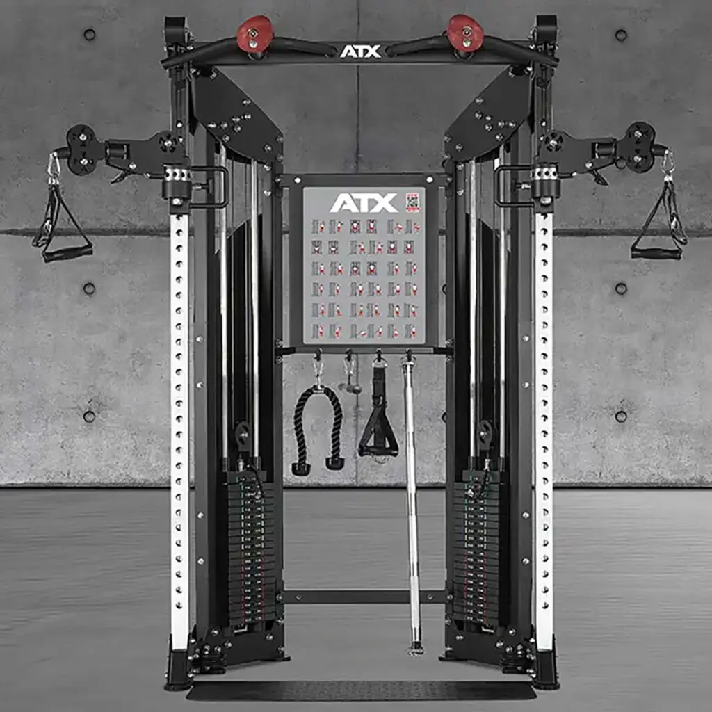 A dual cable crossover machine in a gym setting with adjustable pulleys, weight stacks, and various attachments. The background features a plain concrete wall.