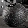 Close-up of an ATX® Slam Ball 8 kg featuring a textured surface for grip, resting on a gym mat with blurred fitness equipment in the background.