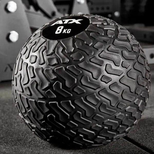 Close-up of an ATX® Slam Ball 8 kg featuring a textured surface for grip, resting on a gym mat with blurred fitness equipment in the background.