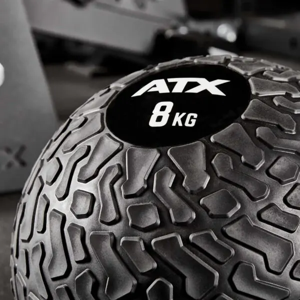 Close-up of a black ATX® Slam Ball labeled 8 KG with a textured surface, set against a blurred gym background.
