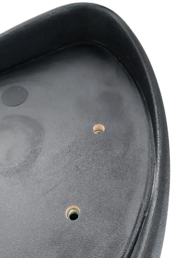Close-up of the underside of a black plastic seat with two visible holes for mounting. The surface has a slight texture, and the edges are slightly raised for reinforcement.