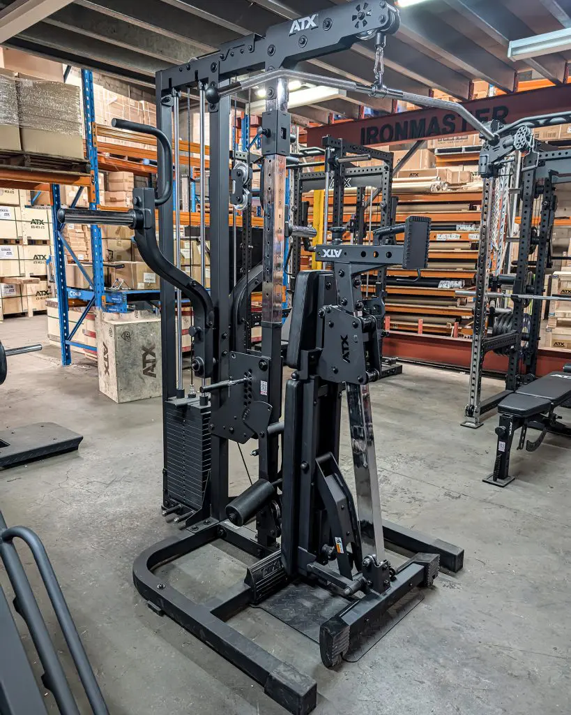 A black ATX multi-functional gym machine stands in a warehouse setting, surrounded by metal shelves, boxes, and other gym equipment.
