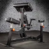 A gym machine with padded supports and handles, designed for seated rows and arm exercises, is positioned next to an ATX® Bicep Blaster Preacher Curl machine against a gray brick wall.