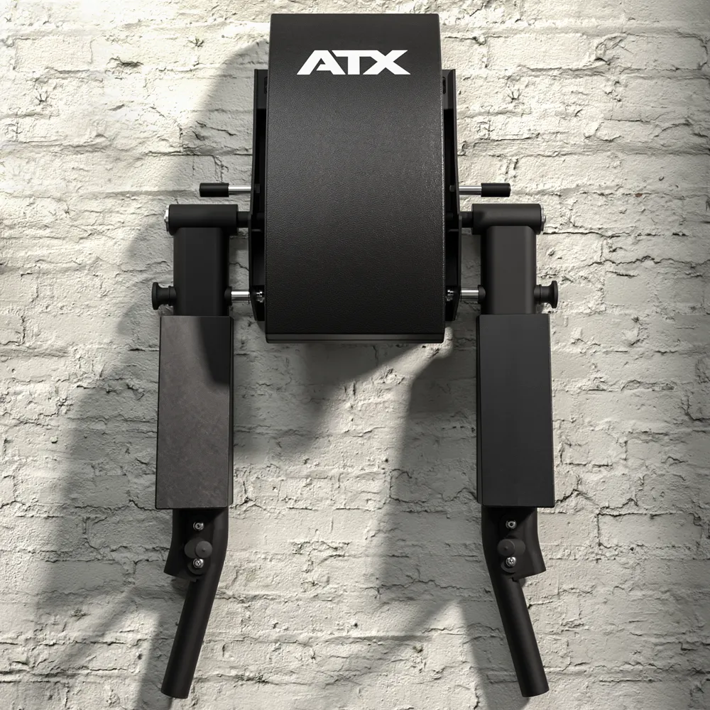 An ATX® Wall Mounted Knee Raise & Dip in black is installed on a white brick wall, featuring two padded arm supports and two downward-angled handles.