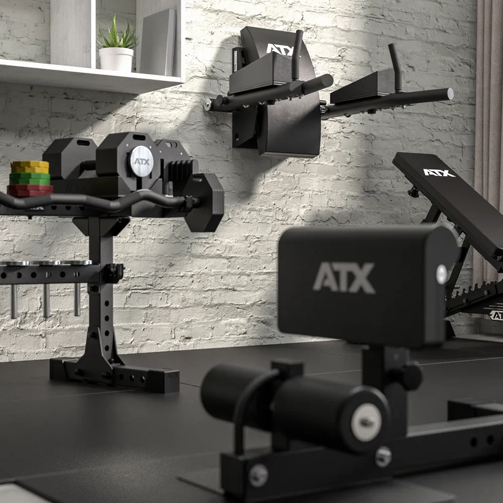 A modern home gym with various black ATX workout equipment, including a bench, weights, and the ATX® Wall Mounted Knee Raise & Dip station, set against a white brick wall.