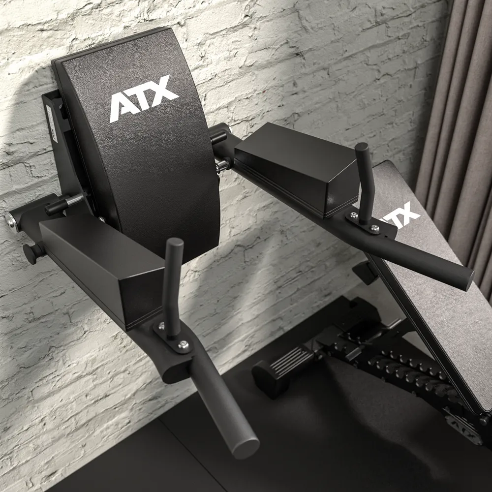 Close-up of the ATX® Wall Mounted Knee Raise & Dip in black, featuring padded surfaces and handles, mounted against a light gray brick wall near a window with curtains.