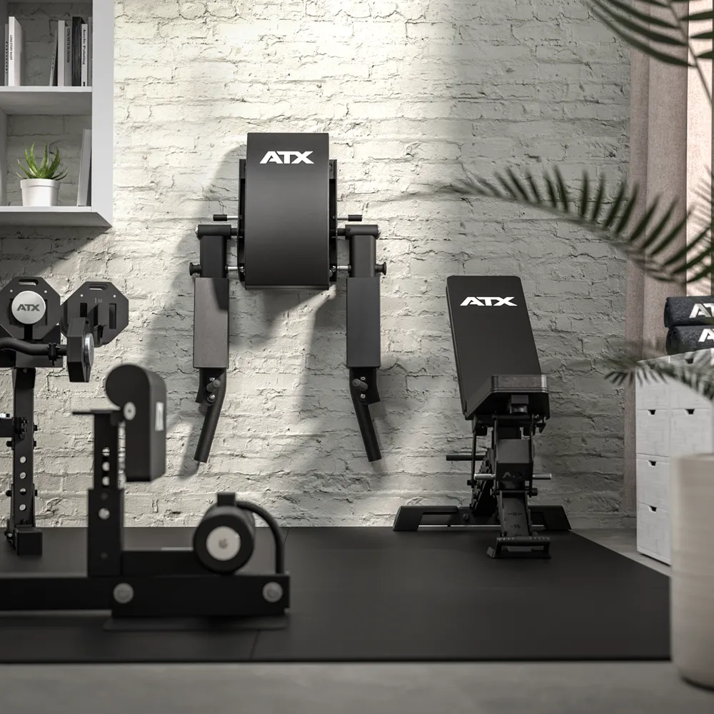 Modern home gym featuring the ATX® Wall Mounted Knee Raise & Dip in black, installed against a light gray brick wall; a potted plant is placed in the foreground, with shelves and drawers visible to the side.