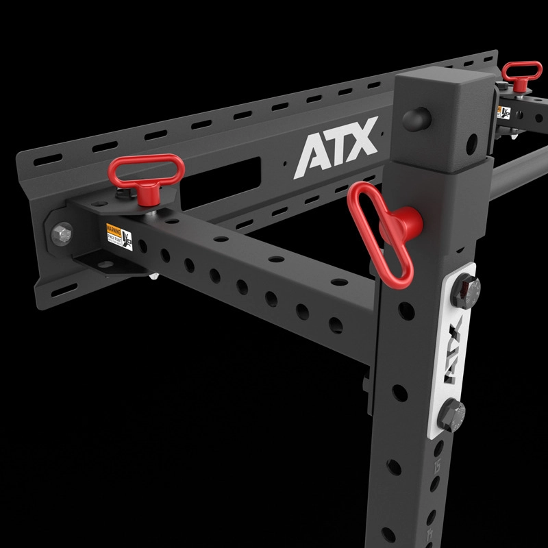 Close-up of the ATX® Fold Back Rack - Wall Mounted, a black metal power rack with multiple holes for adjustable attachments, red locking pins, and ATX branding, displayed against a black background.