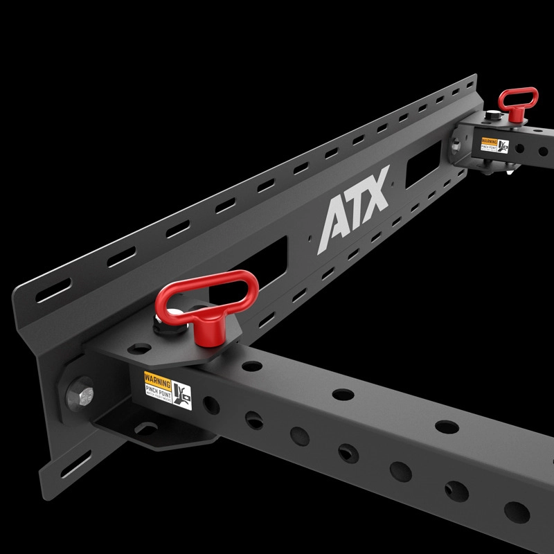 Close-up of the ATX® Fold Back Rack - Wall Mounted, a black metal gym rack attachment with perforated beams and two red safety pins, displayed against a black background. Frame features a warning sticker and ATX branding.