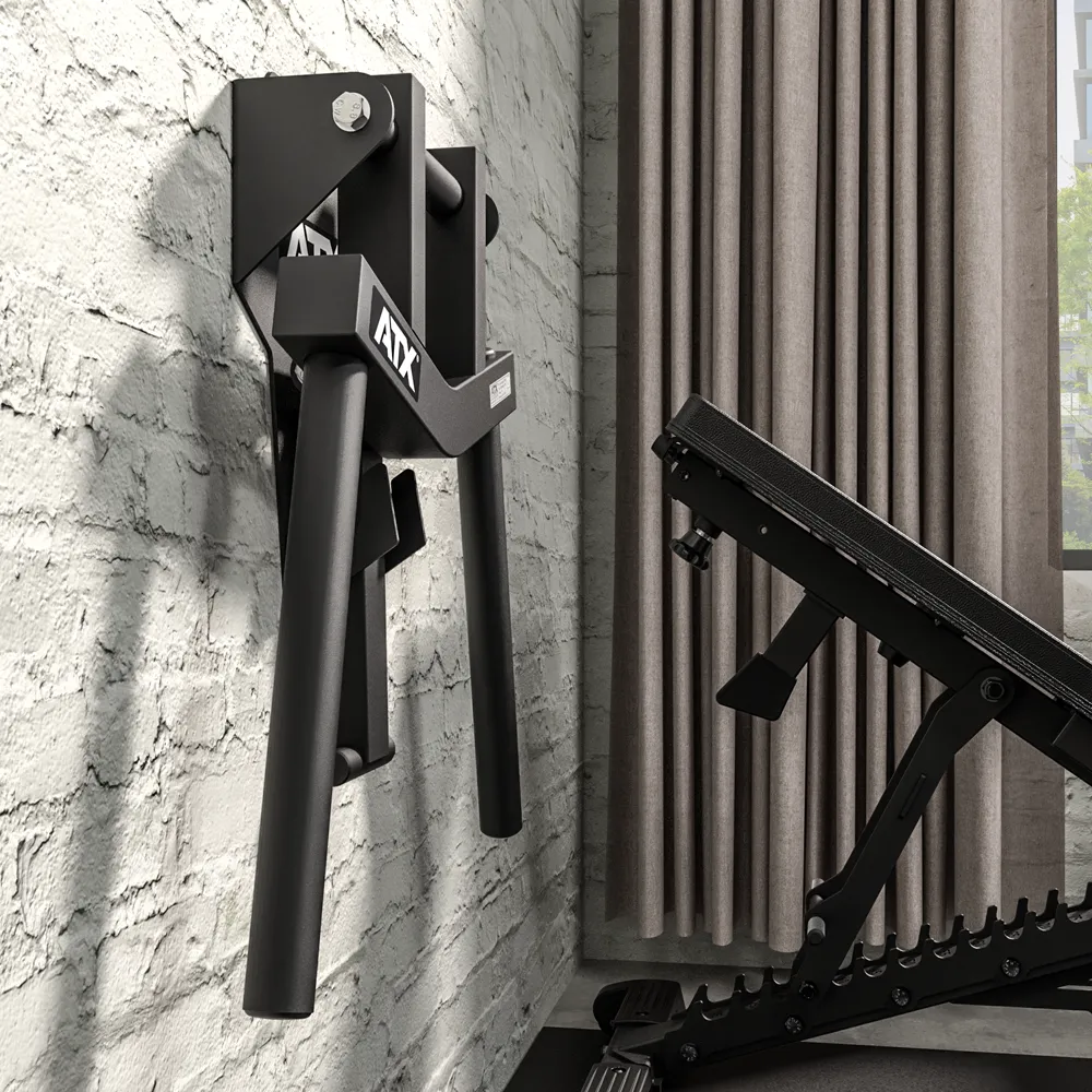 ATX® Folding Wall Mounted Dip Handles are attached to a white brick wall beside a black adjustable workout bench, with tall beige curtains and a window in the background.